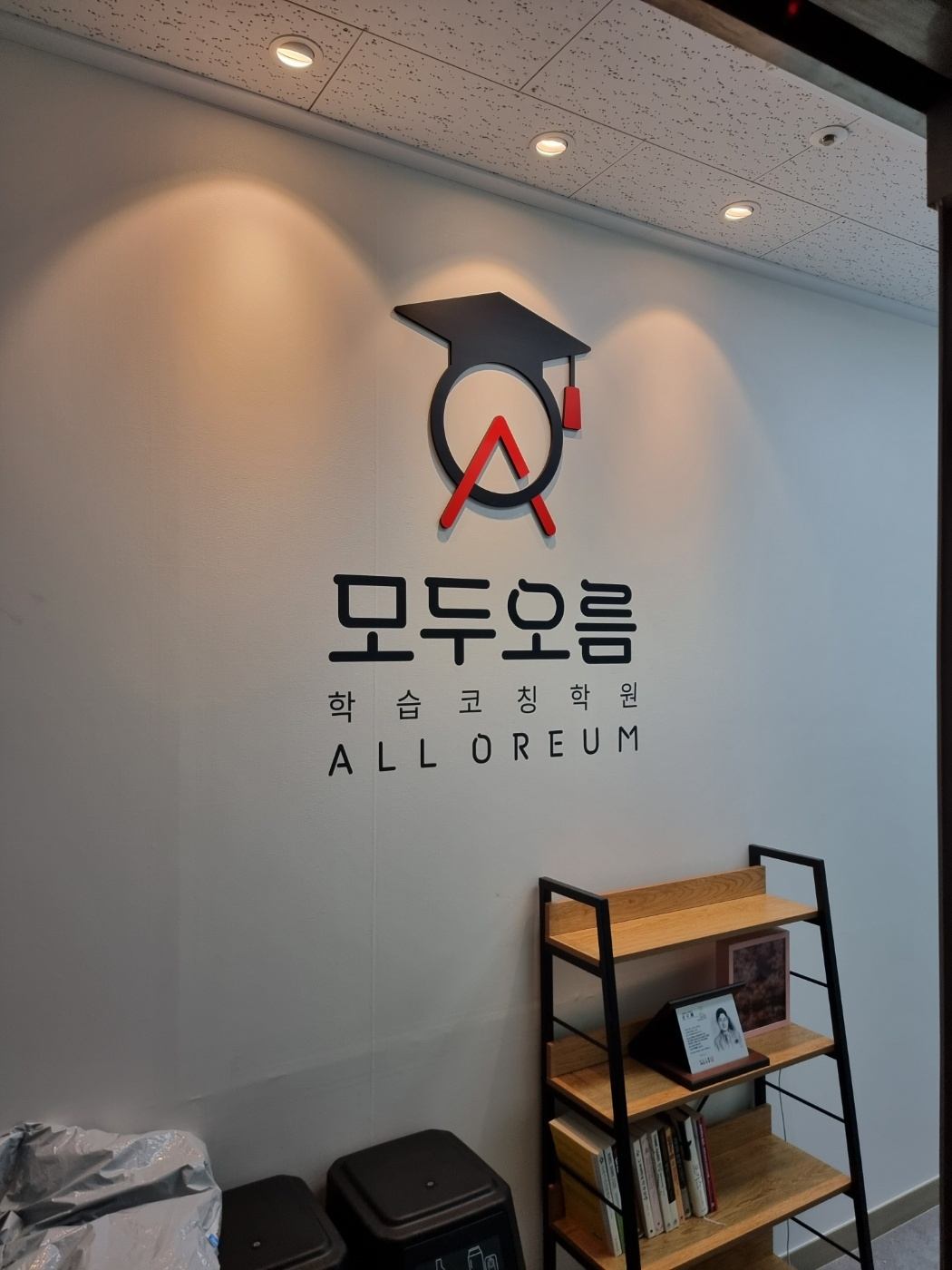 진천점 상담 공간 — 흰 벽에 붙은 모두오름 ALL OREUM 학습코칭학원 로고와 책이 놓인 선반