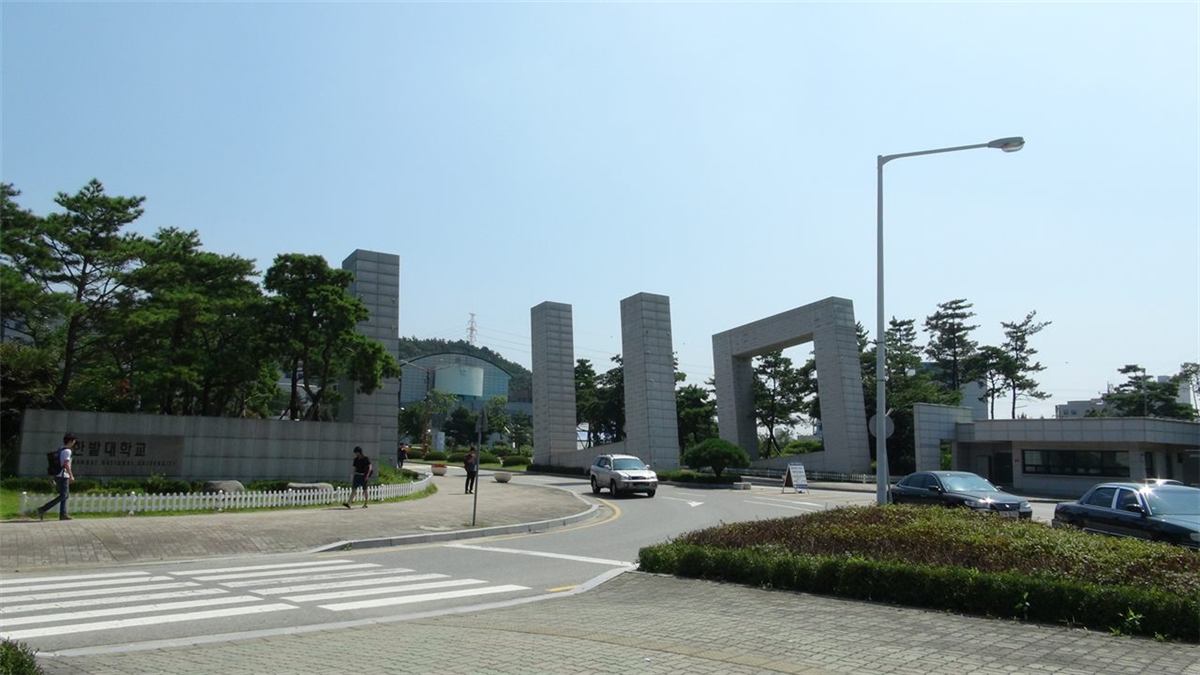 국립한밭대학교 정문 — 화강암 기둥 여러 개가 나란히 선 구조물과 그 옆 낮은 담장에 '한밭대학교'라고 새겨져 있고, 뒤로 소나무와 캠퍼스 건물이 보인다
