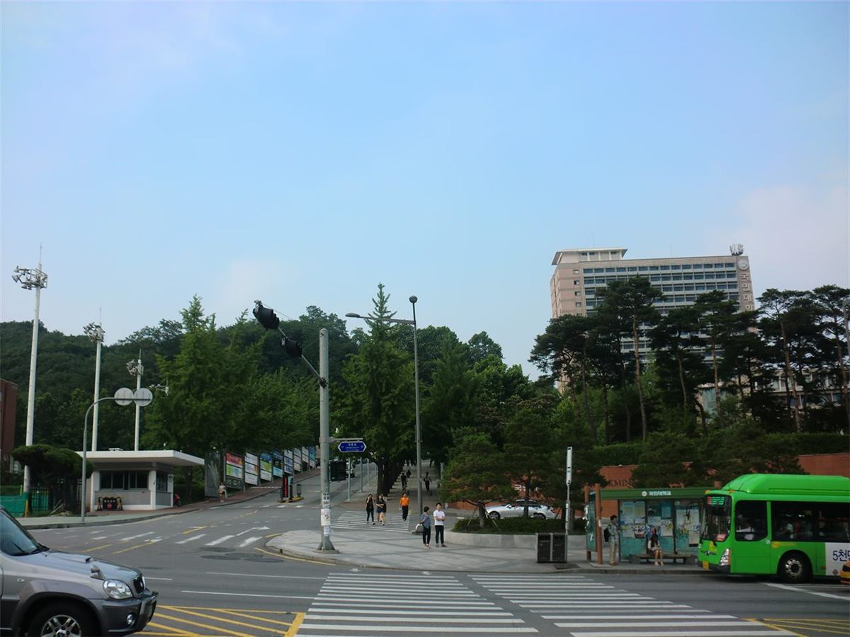 국민대학교 정문 — 돌기둥 위에 국민대학교라고 적힌 표지가 서 있고, 그 뒤로 캠퍼스로 이어지는 오르막길과 나무들이 보인다