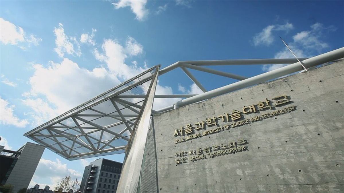 서울과학기술대학교 캠퍼스 입구 — 노출 콘크리트 벽면에 서울과학기술대학교와 SEOUL NATIONAL UNIVERSITY OF SCIENCE AND TECHNOLOGY 금색 글자가 붙어 있고, 그 아래에 서울테크노파크 표기가 함께 있다. 왼쪽으로는 흰색 철골 기둥이 떠받치는 넓은 삼각형 캐노피 지붕이 파란 하늘을 향해 뻗어 있다