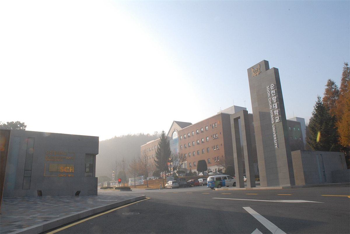 순천향대학교 정문 — 화강암 기둥에 '순천향대학교 SOON CHUN HYANG UNIVERSITY'라고 세로로 새겨져 있고, 왼쪽 낮은 담장에는 'SCH SINCE 1978' 표지가 있다. 뒤로 캠퍼스 건물과 낮은 산이 보인다