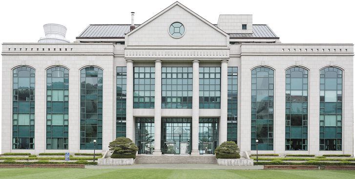 울산대학교 본관 — 가운데 삼각 박공과 원형 창, 흰 기둥이 늘어선 현관, 좌우로 아치형 유리창이 이어진 석조 건물과 앞쪽 잔디밭
